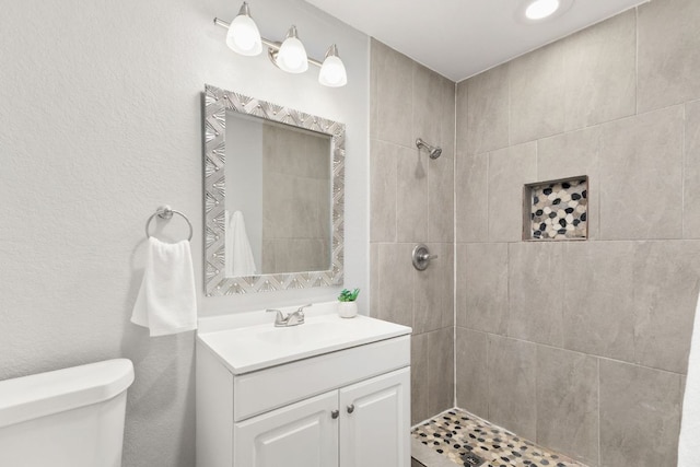 full bathroom featuring vanity, a textured wall, a tile shower, and toilet