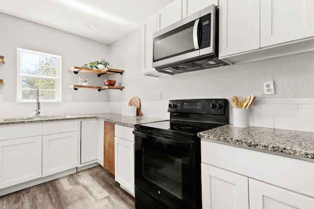 kitchen featuring black electric range oven, stainless steel microwave, white cabinets, a sink, and light wood-style flooring