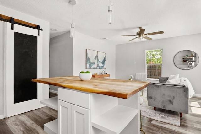 dining space featuring dark wood-type flooring, a ceiling fan, and a barn door