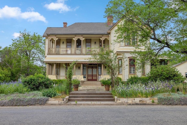 view of front of property featuring covered porch, a chimney, and a balcony