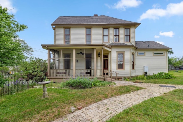 view of front facade with a chimney, a ceiling fan, fence, a front lawn, and a shingled roof