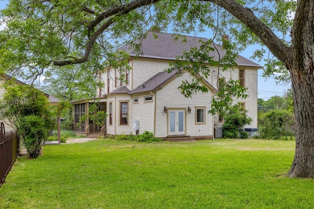 rear view of property featuring a sunroom, a yard, french doors, and fence