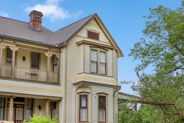 view of front of property featuring a shingled roof, a chimney, and a balcony