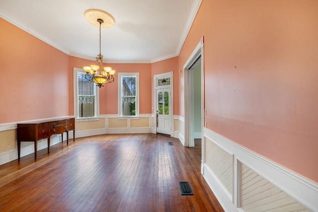 unfurnished dining area featuring visible vents, ornamental molding, wainscoting, dark wood-type flooring, and a notable chandelier
