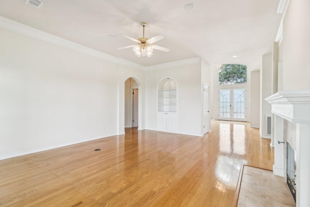 unfurnished living room with visible vents, ornamental molding, light wood-style floors, ceiling fan, and arched walkways
