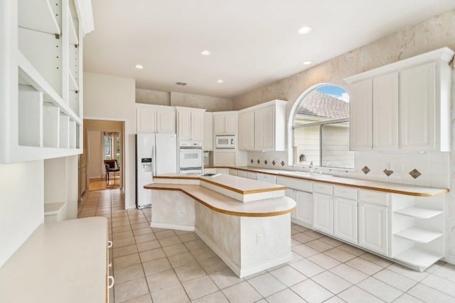 kitchen featuring a sink, light tile patterned floors, a kitchen island, and white appliances