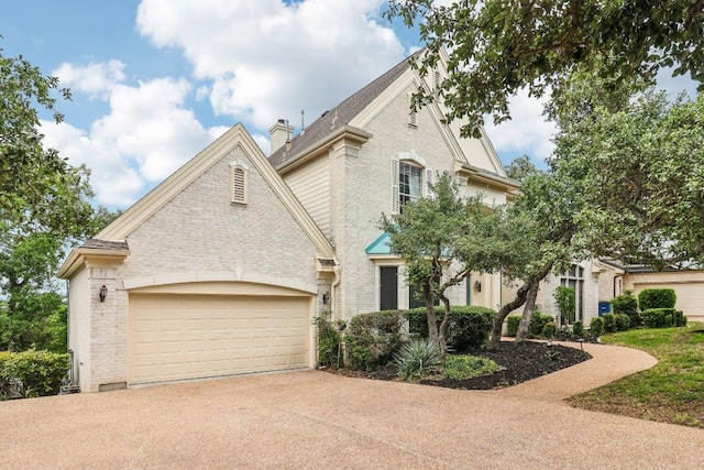 french country inspired facade with a garage, a chimney, driveway, and brick siding