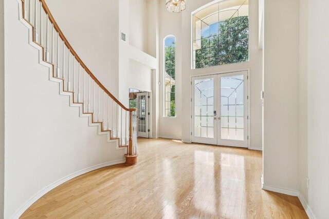 foyer with a high ceiling, a notable chandelier, stairs, wood finished floors, and visible vents