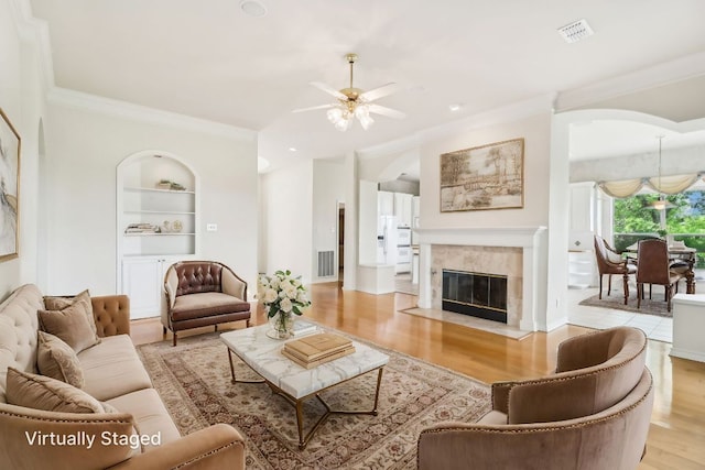 living room featuring visible vents, crown molding, built in shelves, a ceiling fan, and light wood finished floors