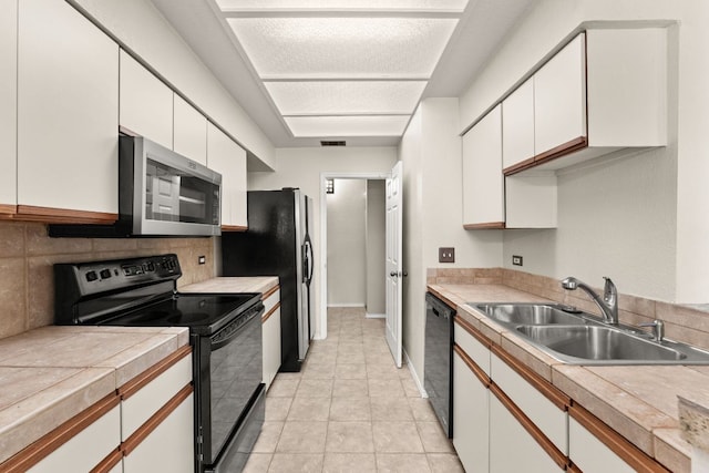 kitchen featuring decorative backsplash, a sink, light countertops, black appliances, and white cabinetry
