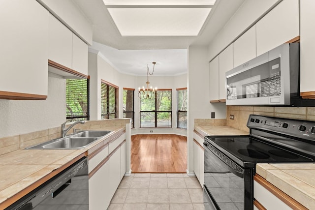 kitchen featuring tile countertops, a sink, white cabinets, black appliances, and a chandelier