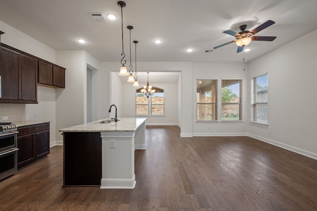 kitchen with visible vents, range with two ovens, light stone counters, a sink, and ceiling fan with notable chandelier
