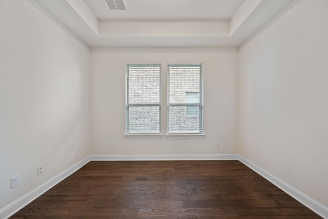 unfurnished room with visible vents, baseboards, dark wood-type flooring, and a tray ceiling