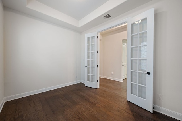 empty room featuring a raised ceiling, french doors, baseboards, dark wood-type flooring, and visible vents