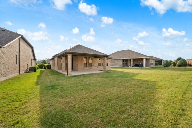 rear view of property with roof with shingles, brick siding, central AC unit, a lawn, and a patio