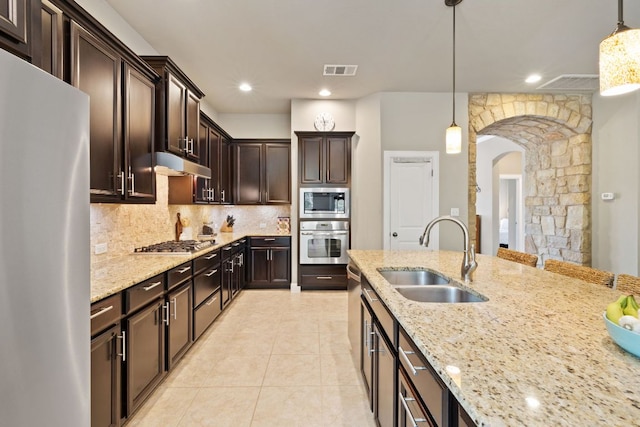 kitchen with visible vents, arched walkways, light stone counters, a sink, and stainless steel appliances