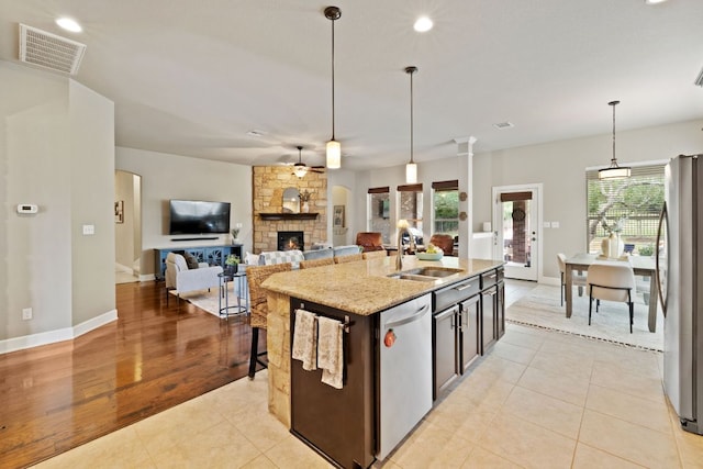 kitchen with appliances with stainless steel finishes, light stone counters, a sink, a fireplace, and visible vents