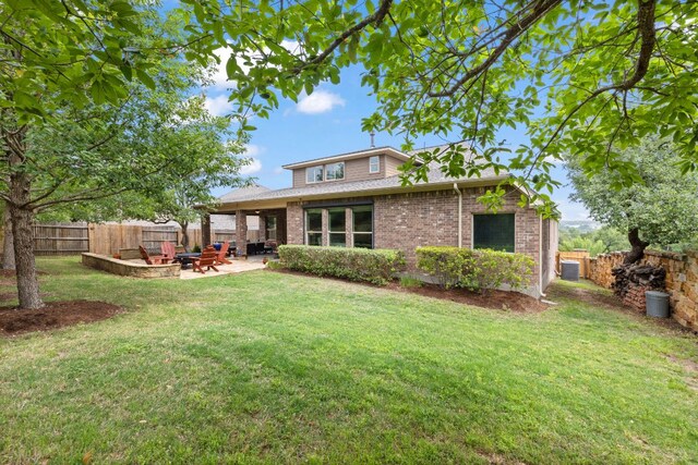 back of property with brick siding, a fenced backyard, a lawn, a patio, and a fire pit