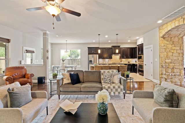 living room featuring visible vents, decorative columns, baseboards, ceiling fan, and light wood-style flooring