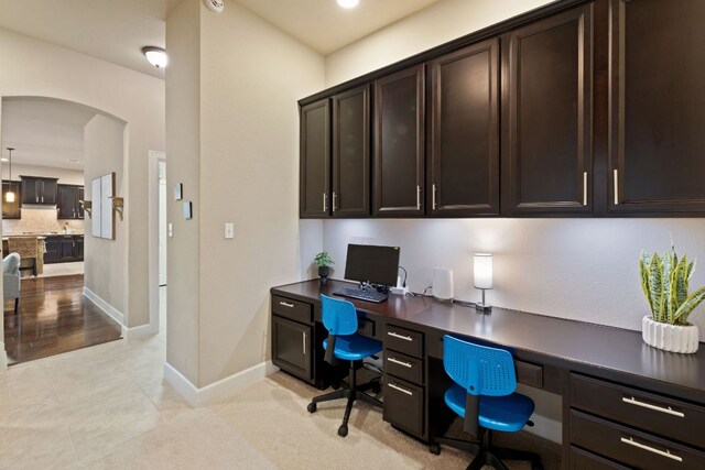 office area featuring arched walkways, baseboards, light tile patterned flooring, and built in desk