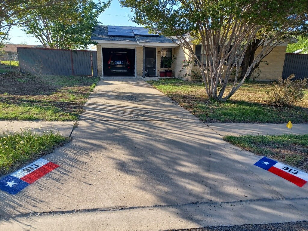 bungalow with roof mounted solar panels, fence, and driveway