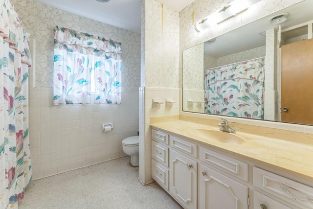 full bath with vanity, wainscoting, toilet, tile walls, and wallpapered walls