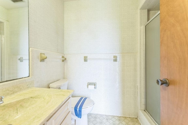 bathroom featuring vanity, toilet, tile walls, a shower stall, and visible vents