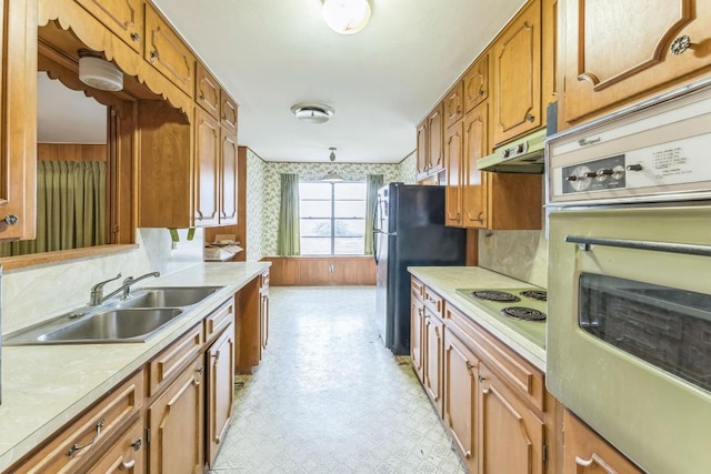 kitchen featuring brown cabinetry, a sink, white appliances, and light countertops