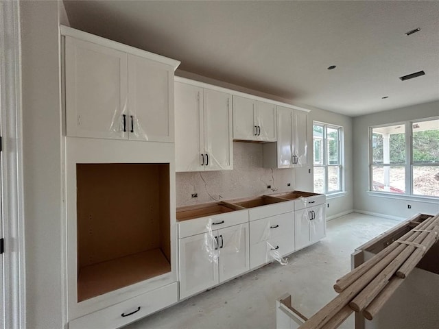 kitchen with baseboards, decorative backsplash, concrete flooring, and white cabinets