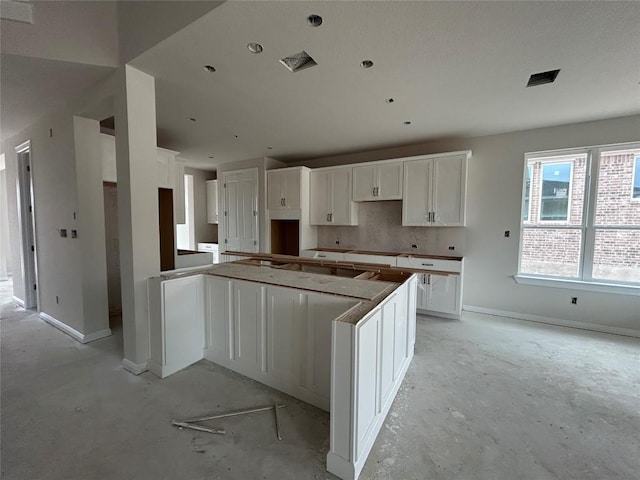 kitchen with unfinished concrete floors, baseboards, and white cabinetry