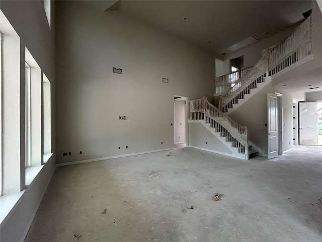 unfurnished living room featuring a high ceiling, unfinished concrete flooring, and stairs