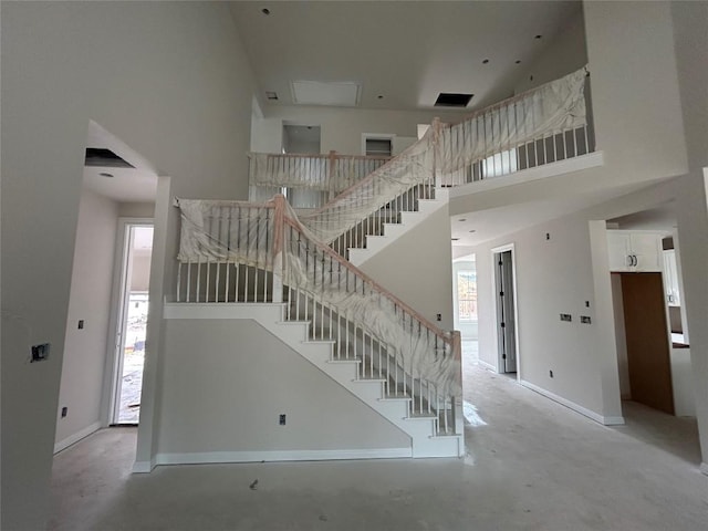 stairs featuring baseboards, a high ceiling, and concrete flooring