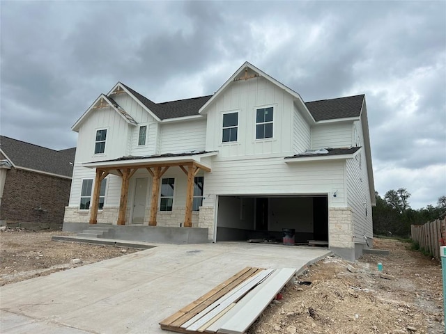 modern farmhouse featuring board and batten siding, covered porch, driveway, an attached garage, and stone siding