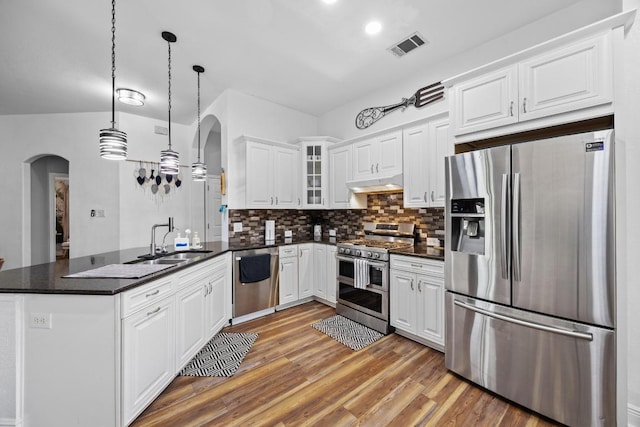 kitchen with arched walkways, appliances with stainless steel finishes, under cabinet range hood, and a peninsula