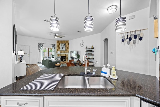 kitchen with ceiling fan, visible vents, arched walkways, a sink, and dark stone countertops
