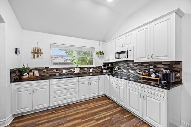 kitchen featuring dark countertops, white microwave, dark wood-style floors, tasteful backsplash, and vaulted ceiling