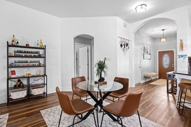 dining area featuring dark wood-style flooring, arched walkways, and baseboards