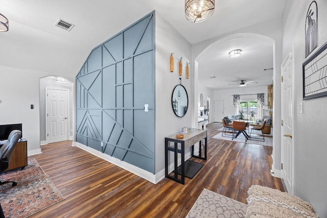hallway featuring visible vents, arched walkways, baseboards, and wood finished floors