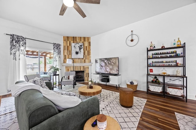 living room featuring baseboards, a ceiling fan, a large fireplace, and wood finished floors