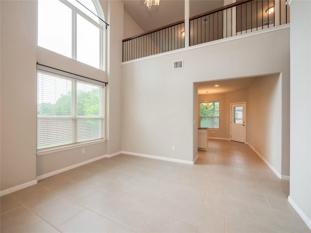 spare room with visible vents, an inviting chandelier, light tile patterned flooring, baseboards, and a high ceiling