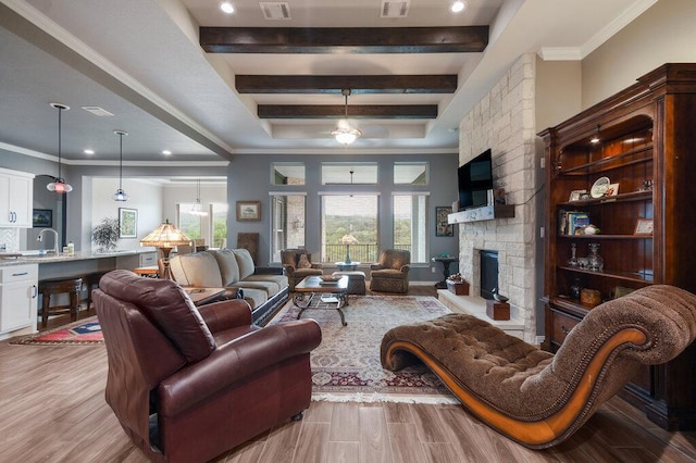 living room featuring crown molding, a stone fireplace, light wood-style flooring, and a raised ceiling