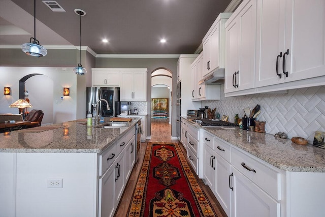 kitchen featuring visible vents, arched walkways, a sink, and under cabinet range hood