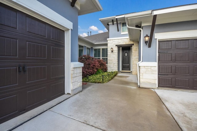 entrance to property with concrete driveway, a garage, stone siding, and stucco siding