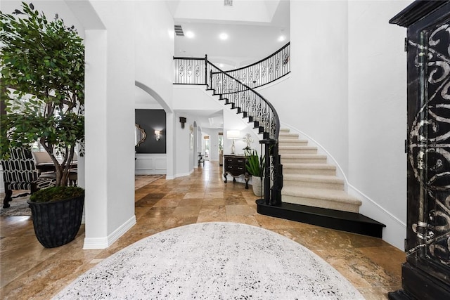 entryway with baseboards, a high ceiling, stairway, arched walkways, and stone finish flooring