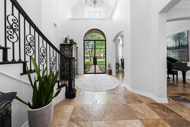 foyer entrance featuring stone tile flooring, an inviting chandelier, baseboards, a high ceiling, and arched walkways