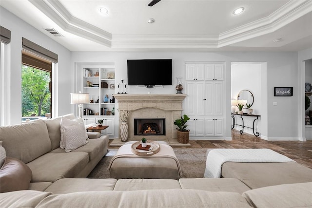 living area with crown molding, a tray ceiling, built in shelves, and visible vents
