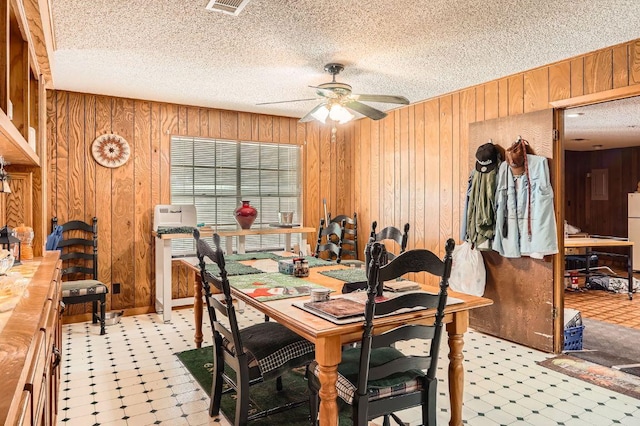 dining area featuring wooden walls, tile patterned floors, a textured ceiling, a ceiling fan, and visible vents