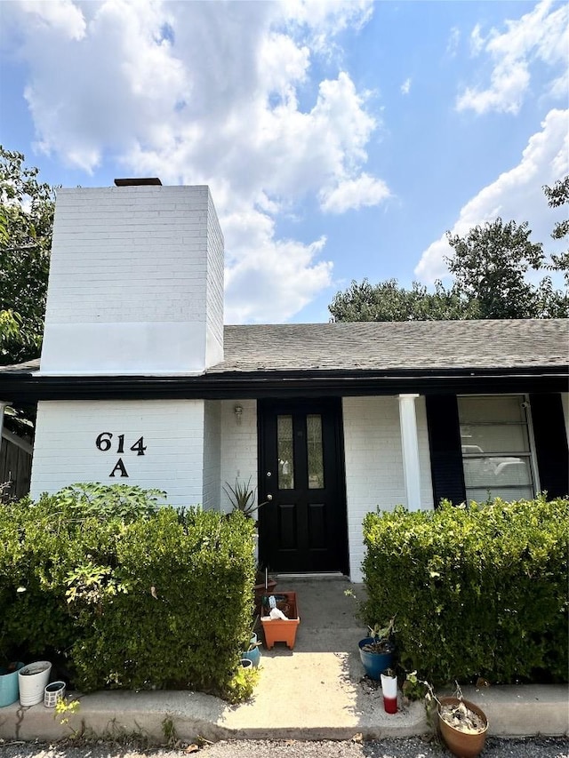 view of exterior entry featuring brick siding and roof with shingles