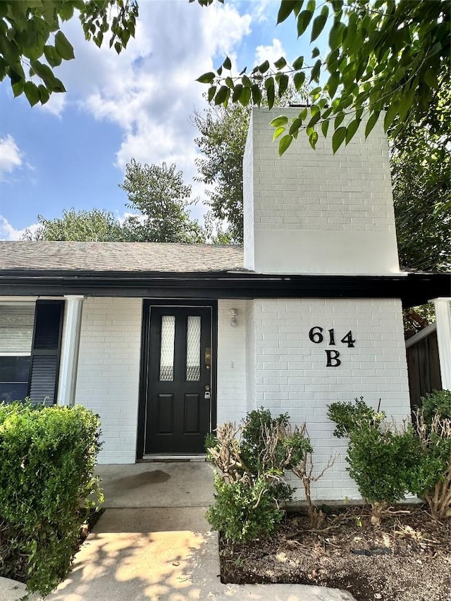property entrance with roof with shingles and brick siding