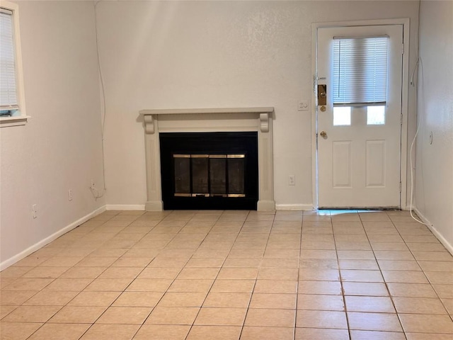 unfurnished living room with baseboards, a glass covered fireplace, and light tile patterned floors